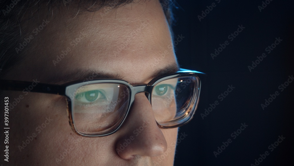 Closeup of man eyes in eyeglasses in front of the computer, concentrated look. Young man sitting working alone at night Closeup of man eyes in eyeglasses in front of the computer, concentrated look. Young man sitting working alone at night