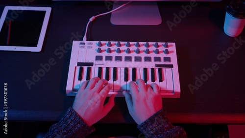 Closeup of hands composing music in night using midi controller. Top view of person playing music with electronic keyboard, midi keys on the table with neon lights