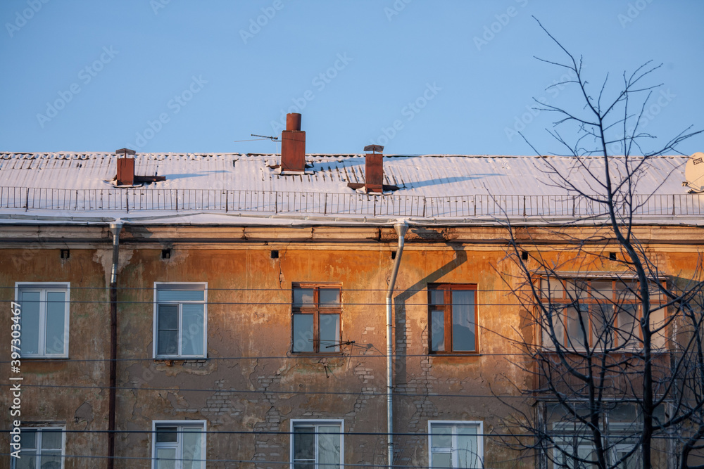 Windows of an old brick house close-up in the rays of the rising sun. Top floor, drainpipe. The roof of the house is covered with snow. Chimneys. Windows of an old brick house close-up in the rays of the rising sun. Top floor, drainpipe. The roof of the house is covered with snow. Chimneys.