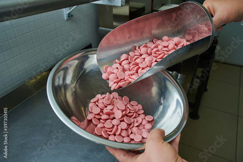 Chocolate colored pink in a metal scoop in the hands of a pastry chef against the background of fine-grain production chocolate candies and confectionery