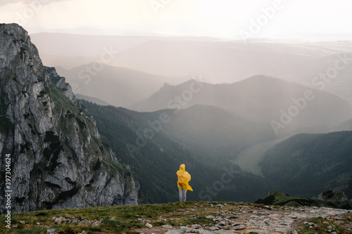 Anonymous tourist in yellow raincoat hiking in mountain during a thunderstorm photo