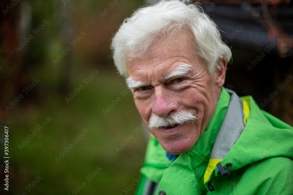 Outdoor portrait of a handsome smiling senior man wearing a casual green jacket over the autumn background.