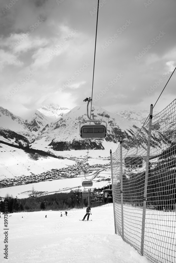 Fototapeta premium Chair-lift, snowy ski slope with snowboarders and skiers in high mountains