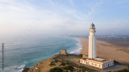 Drone views of the Trafalgar Lighthouse on the Costa de la Luz in Caños de Meca, Cadiz Andalucia, Spain. Faro de Trafalgar from above on a beautiful day with clouds and the blue sea.