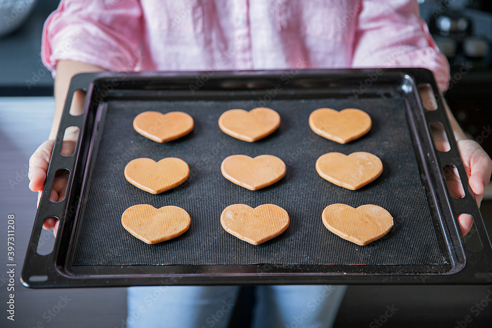 Female hands hold a black baking sheet with gingerbread Female hands hold a black baking sheet with gingerbread