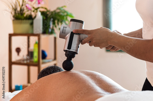 unrecognizable Female therapist using massage gun on back of client