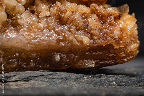 primer plano macro de baklava pastel típico y tradicional turco masa hojaldrada y nuez y pistacho triturado con miel y almíbar de azúcar sobre plato de piedra laja negra