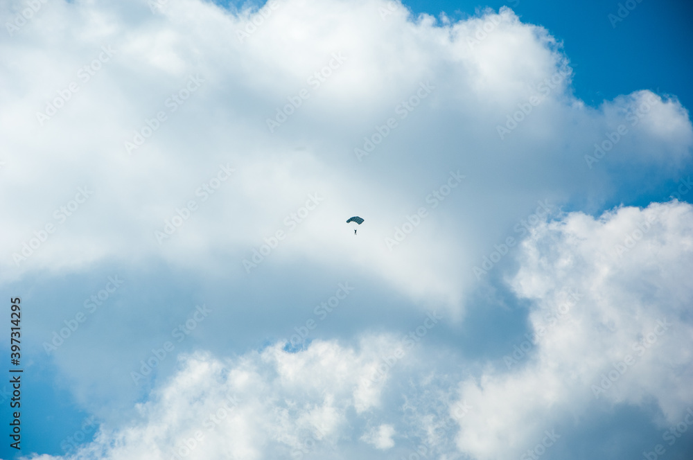 Paratrooper parachuting against white clouds