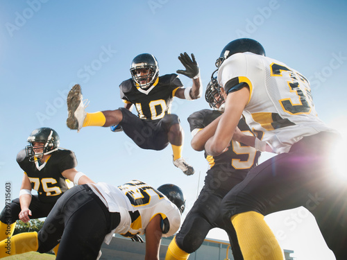 Football player leaping over players on football field
