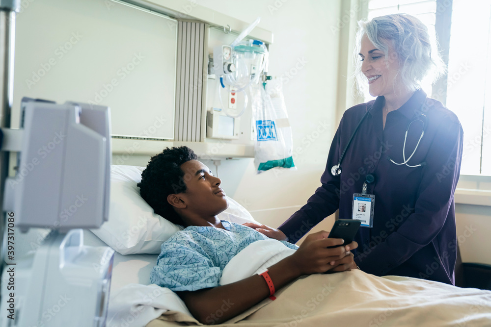 Doctor comforting boy in hospital bed holding cell phone Doctor comforting boy in hospital bed holding cell phone