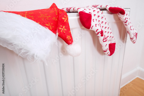 White and red christmas socks and santa hat hanging on warm central heat radiator, winter holiday home mood