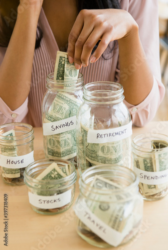 Mixed race woman putting money in savings jars