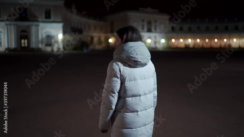 Young adult woman in warm coat walking on an empty dark street at cold night. Pavlovsk Park and Palace in autumn, St. Petersburg, Russia. photo