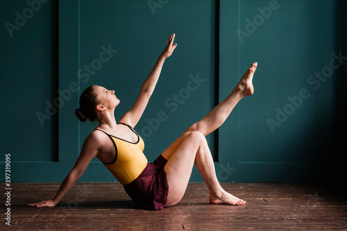 Ballerina in dark bodysuit, in dress in dark interior Studio. Wall of bricks, piano.