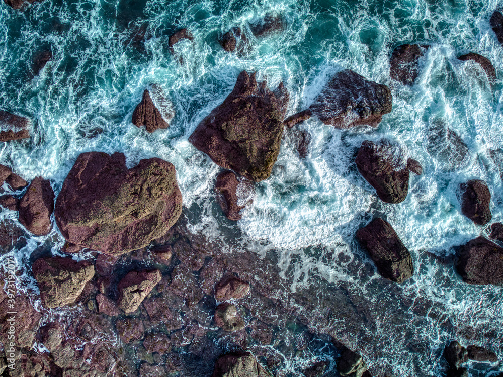 Aerial top view of sea waves hitting rocks.