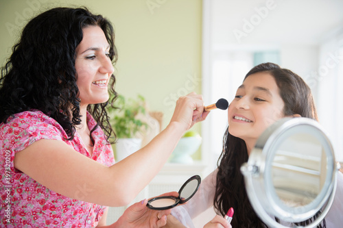 Hispanic mother helping daughter apply makeup