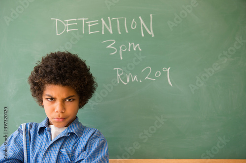 Angry mixed race boy frowning in classroom detention