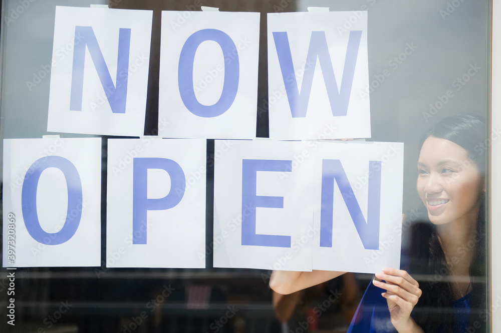 Woman hanging now open sign in store window Woman hanging now open sign in store window
