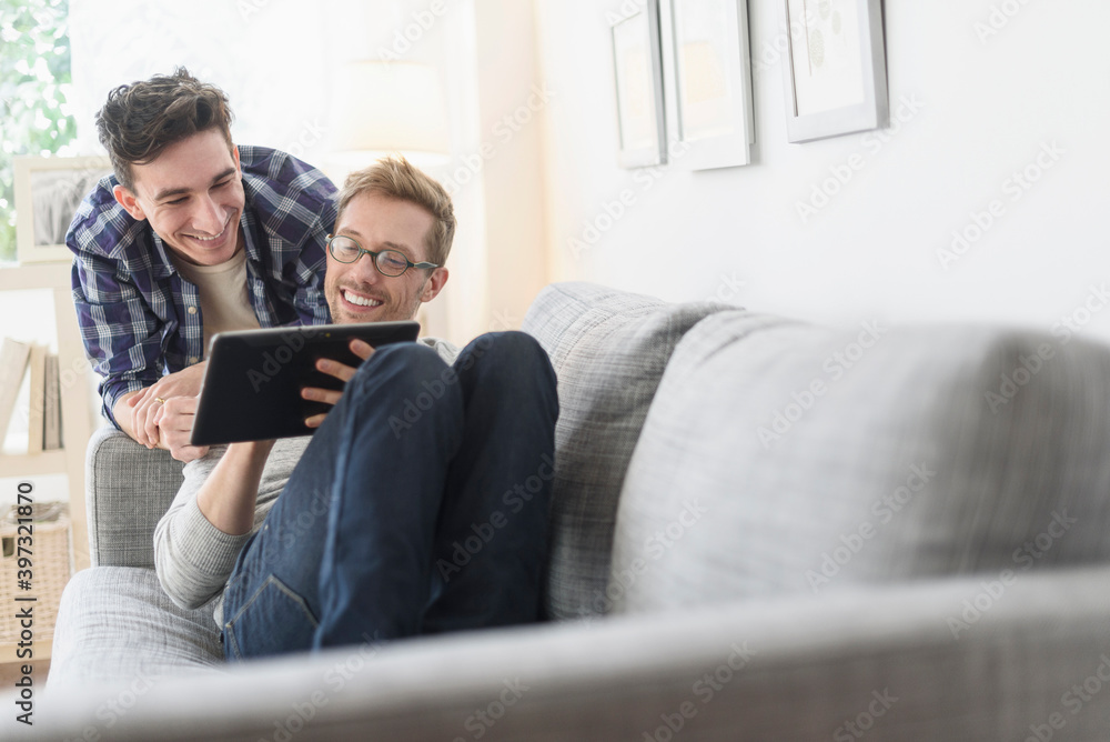 Caucasian gay couple using digital tablet on sofa Caucasian gay couple using digital tablet on sofa