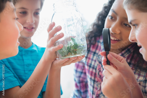 Children examining seeds in jar with magnifying glass