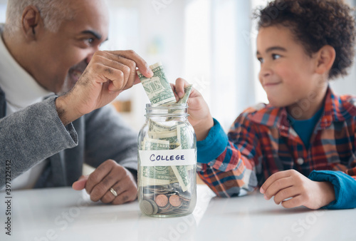 Mixed race grandfather and grandson saving money in college fund jar photo