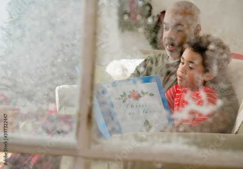 Mixed race grandfather reading to grandson behind window at Christmas