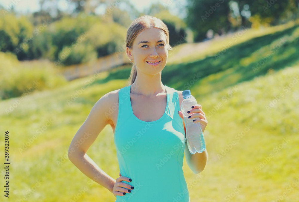 Fitness woman drinking water from bottle on the grass in summer day Fitness woman drinking water from bottle on the grass in summer day