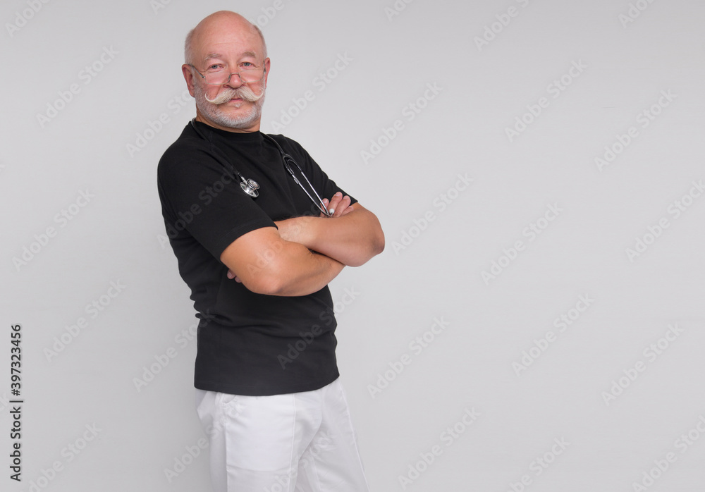 old stylish male doctor in black t-shirt is standing straight with stethoscope on neck with hands crossed in front on white wall background. medical concept. free space on right side, mockup old stylish male doctor in black t-shirt is standing straight with stethoscope on neck with hands crossed in front on white wall background. medical concept. free space on right side, mockup