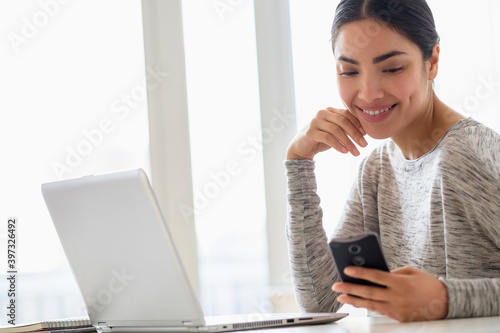 Hispanic woman using cell phone and laptop