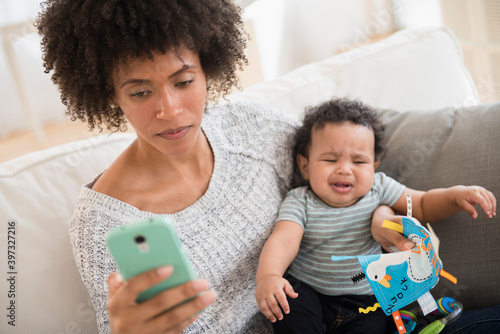 Mother holding crying baby son while texting on cell phone photo