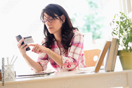 Hispanic woman using credit card with cell phone in home office photo