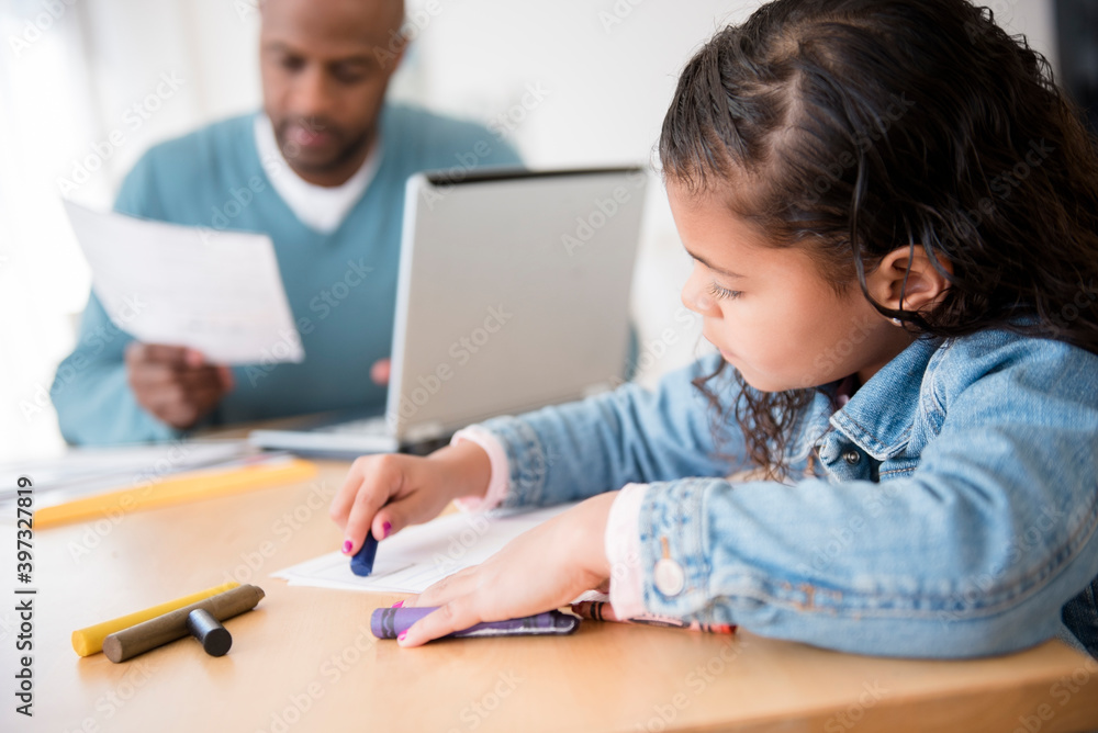 Daughter coloring with crayons while father uses laptop Daughter coloring with crayons while father uses laptop