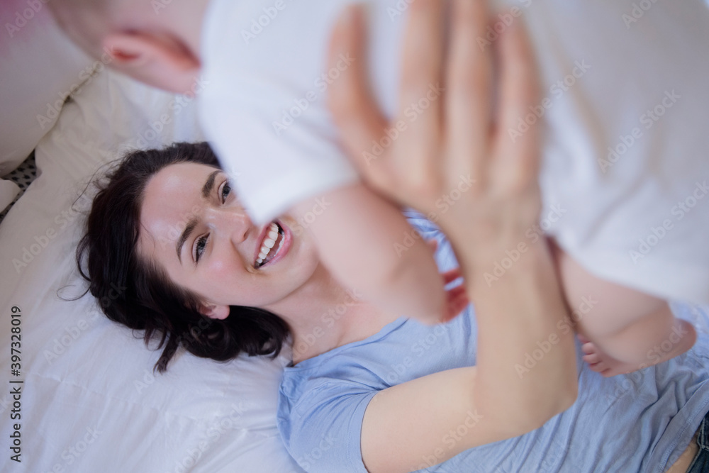 Caucasian mother laying on bed lifting baby son Caucasian mother laying on bed lifting baby son