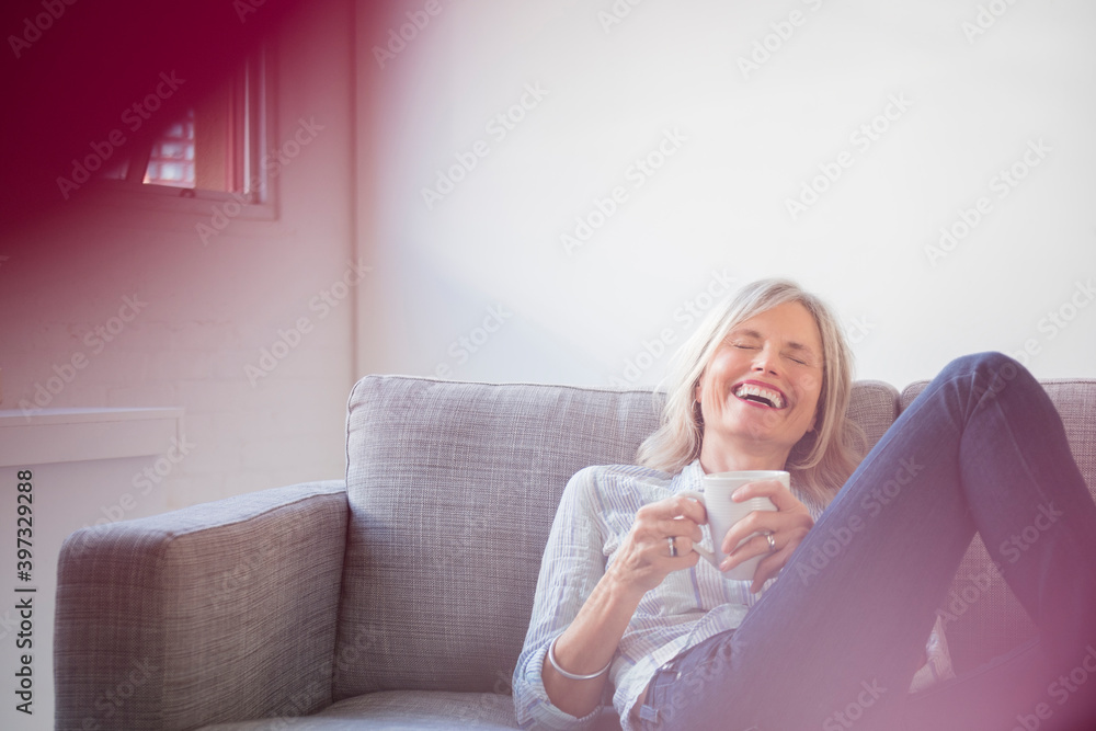 Laughing Caucasian woman sitting on sofa drinking coffee Laughing Caucasian woman sitting on sofa drinking coffee