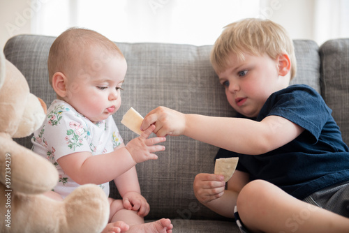 Brother (2-3) sharing crackers with baby sister (12-17 months) photo