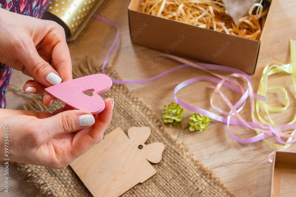 Girl with pink heart, colorful ribbons, wrapping paper and gift box. Preparation for winter holidays. Gift box for Valentines day. Christmas decoration concept. Girls hands with decorating materials.