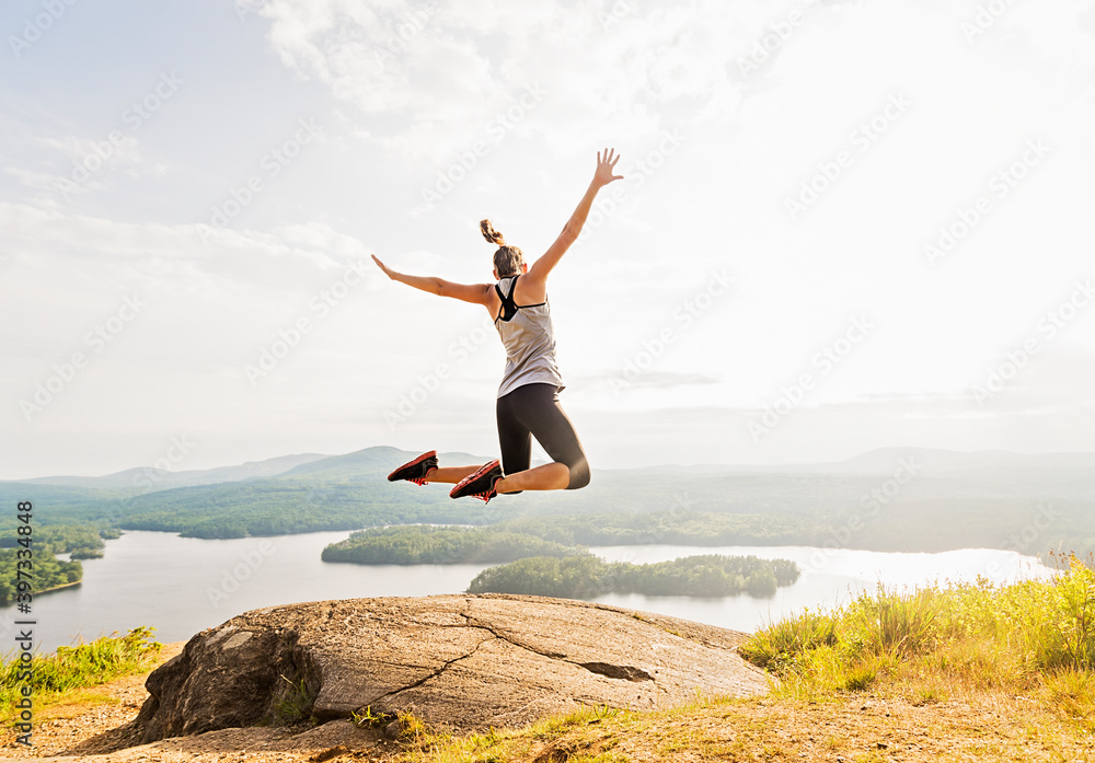 Young woman jumping over mountain top, rear view Young woman jumping over mountain top, rear view