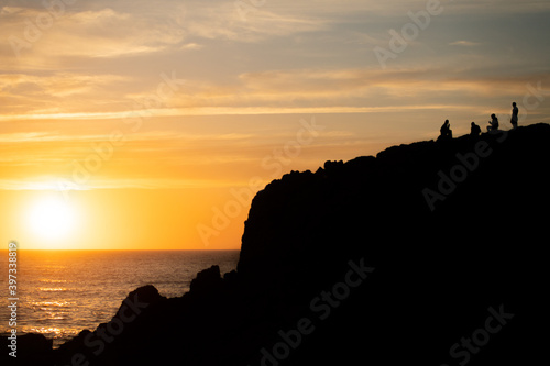 Silhouette of a group of person sitting on a mountain at sunset