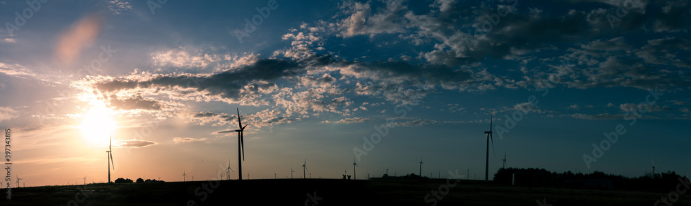 Obraz premium Panorama shot of colorful sky with sun behind the clouds and wind power plants in america
