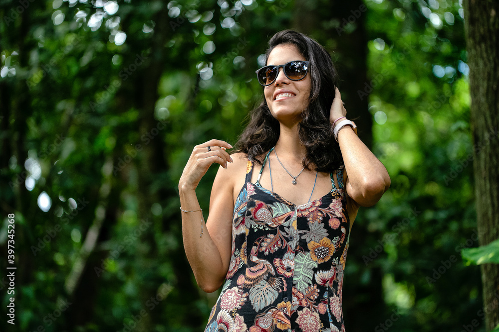 The brunette girl and the rainforest. A woman walks in the rain forest in the late afternoon wearing dark glasses and a casual dress with flower print. Smile. Leisure. healthy life. Lifestyle.