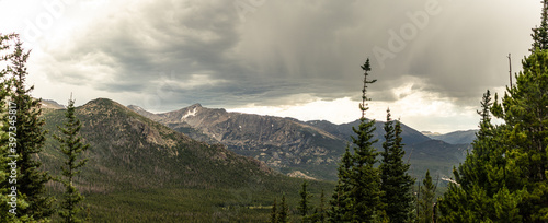 Panorama shot of green rocky hills with remaints of snow and storm clouds in Rocky mountains national park in america