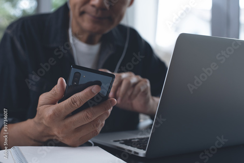 Casual business man making video call using online meeting app via mobile phone and working on laptop computer at home office