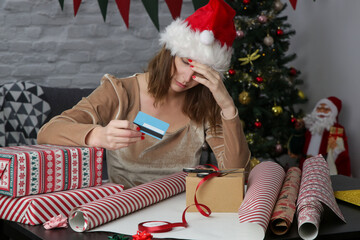 Depressed frustrated woman wrapping Christmas gift boxes thinking about expenses and overspending during winter holidays. Winter holiday stress concept.