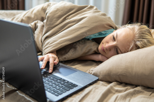 Teenage girl lies in bed and works on laptop. Distance education theme