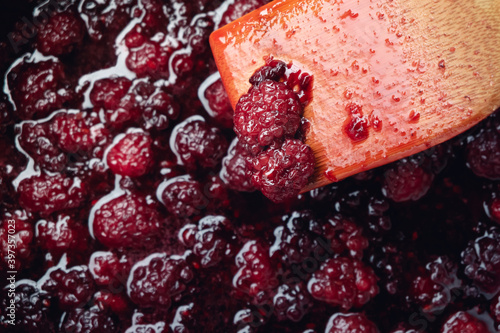 Close up of stirring blackberries and sugar making homemade blackberry jam with wooden utensil.