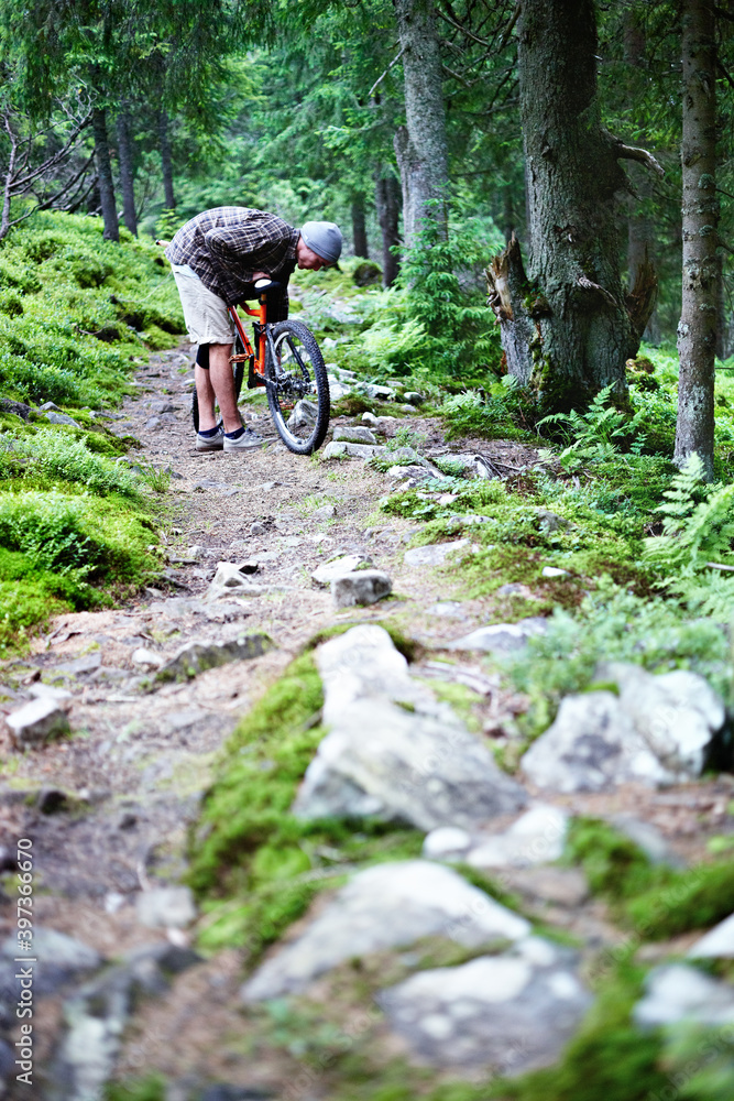 Young caucasian cyclist repairs a mountain bike in the mountains in the forest.