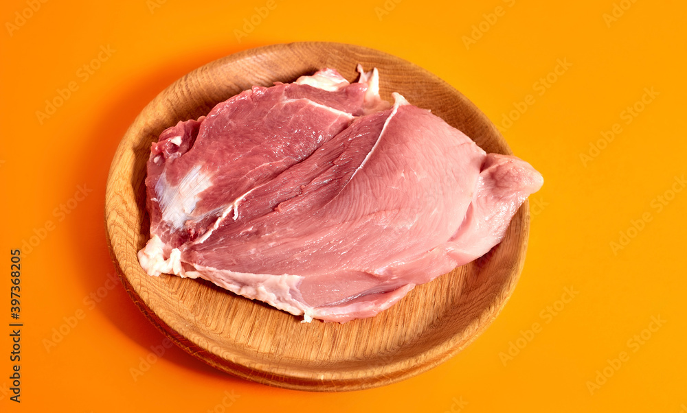 A plate of raw pork meat on an orange background