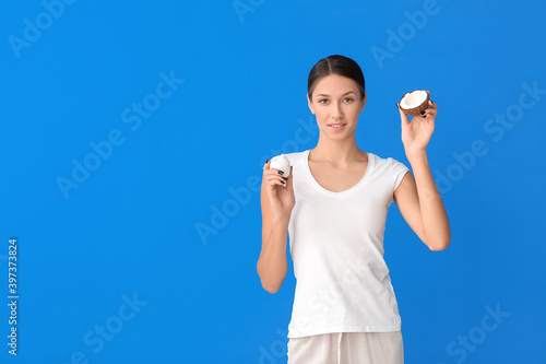 Beautiful young woman with coconut and cream on color background