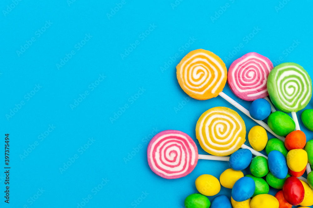 Lollipops on stick and multicolor dragee on blue. Space for text. Top view.