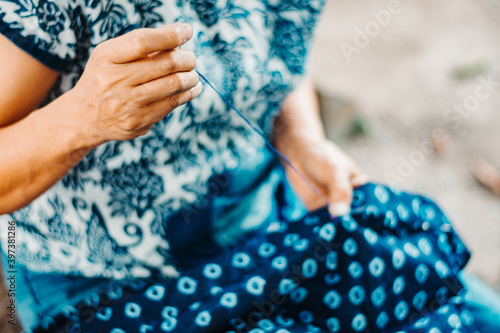 Woman's hands sewing running stitch in blue tribal fabric (dyed indigo color). folk art, crafts.